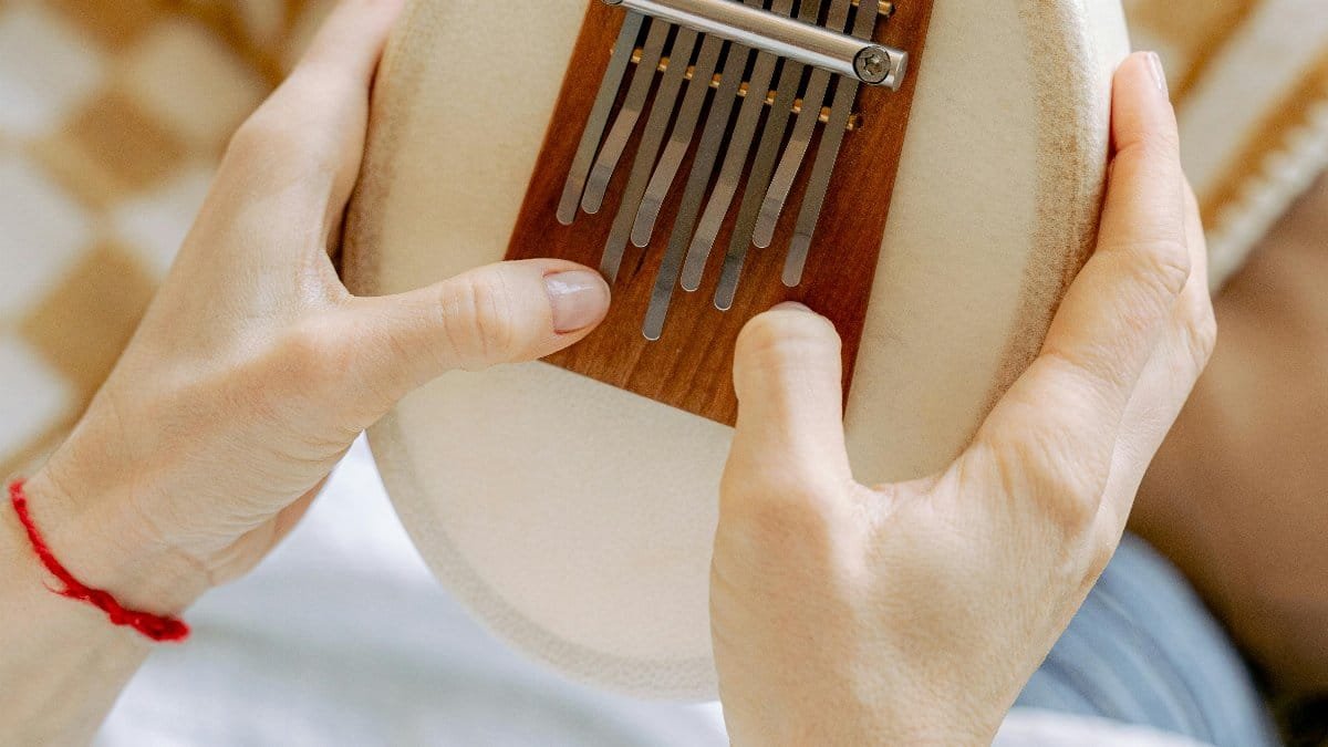 A detailed view of hands playing a kalimba, highlighting the musical instrument and finger movements. via Pexels