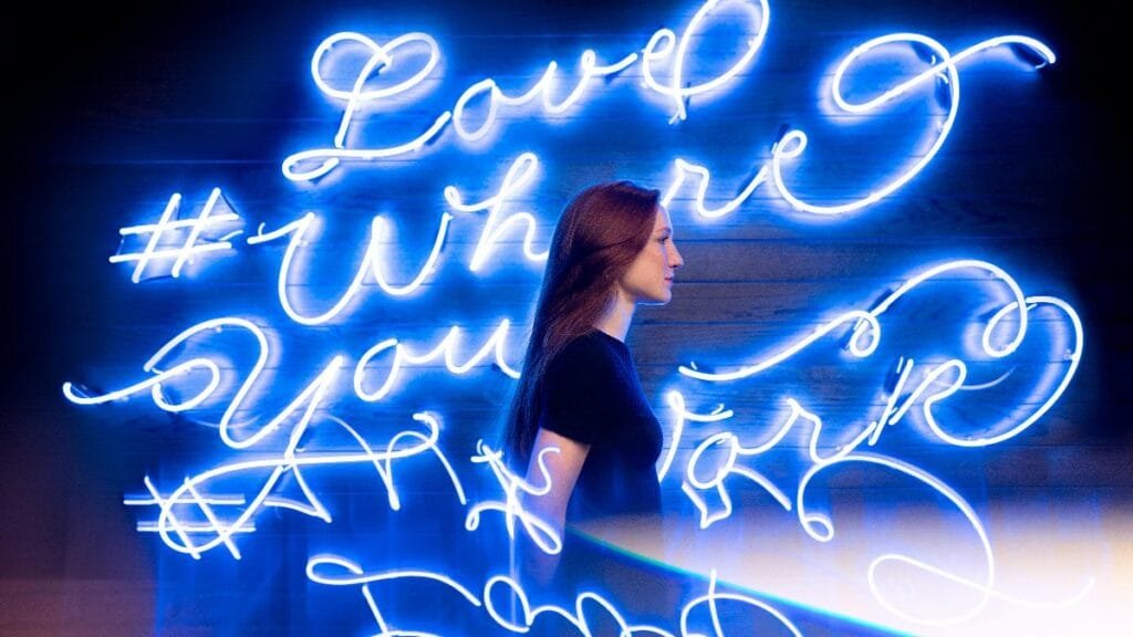 Creative portrait of a woman with neon sign 'Love Where You Work' in blue light. via Pexels