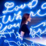 Creative portrait of a woman with neon sign 'Love Where You Work' in blue light. via Pexels