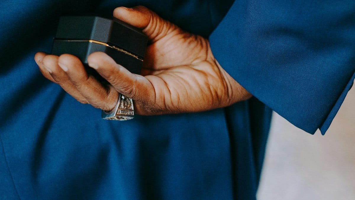 Man in blue suit holding an engagement ring box behind his back, symbolizing a surprise proposal. via Pexels