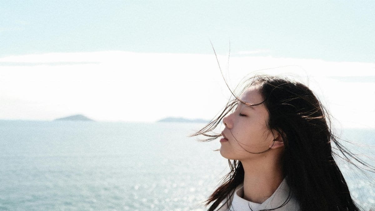 A serene moment with a woman enjoying the sea breeze under a clear sky. via Pexels