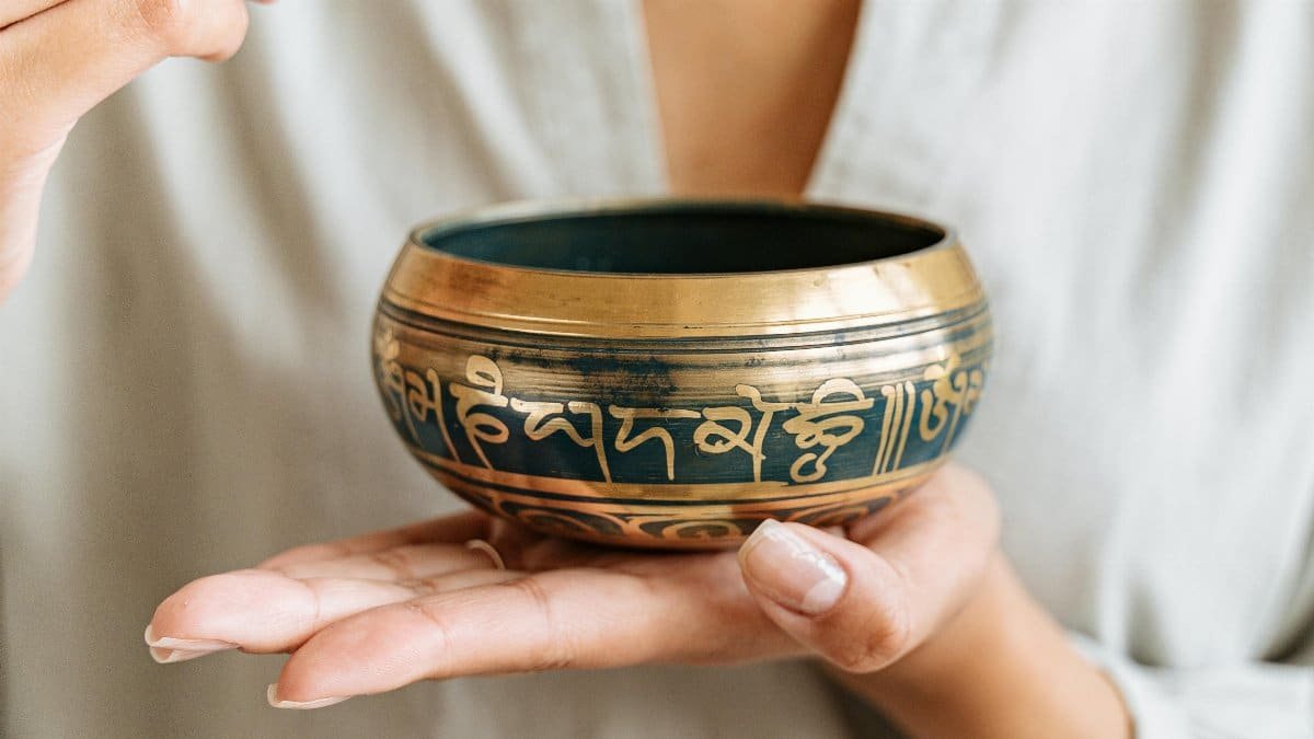 A close-up of hands holding and playing a Tibetan singing bowl, promoting relaxation. via Pexels