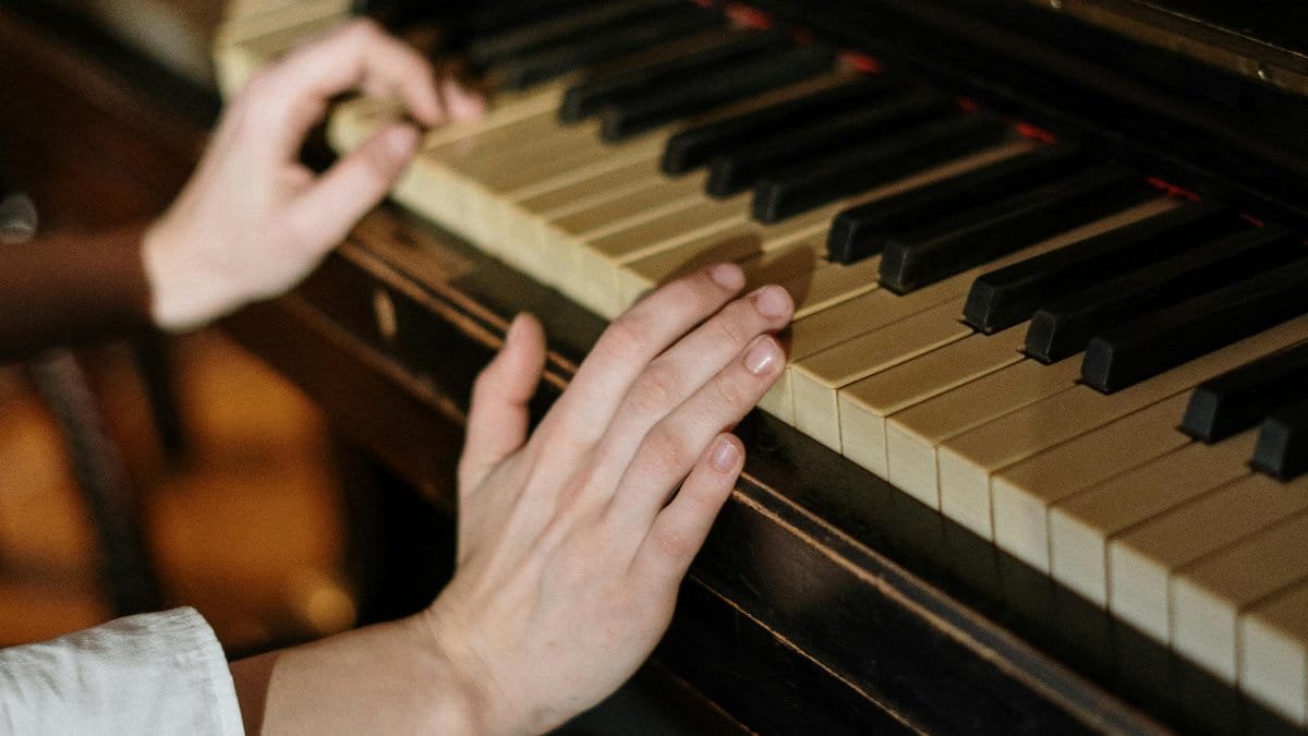 A person playing piano keys indoors, creating a warm, cozy atmosphere. via Pexels