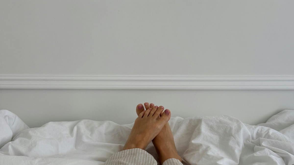 Relaxing morning in bed with legs covered in pajamas on white sheets. Tranquil indoor setting. via Pexels