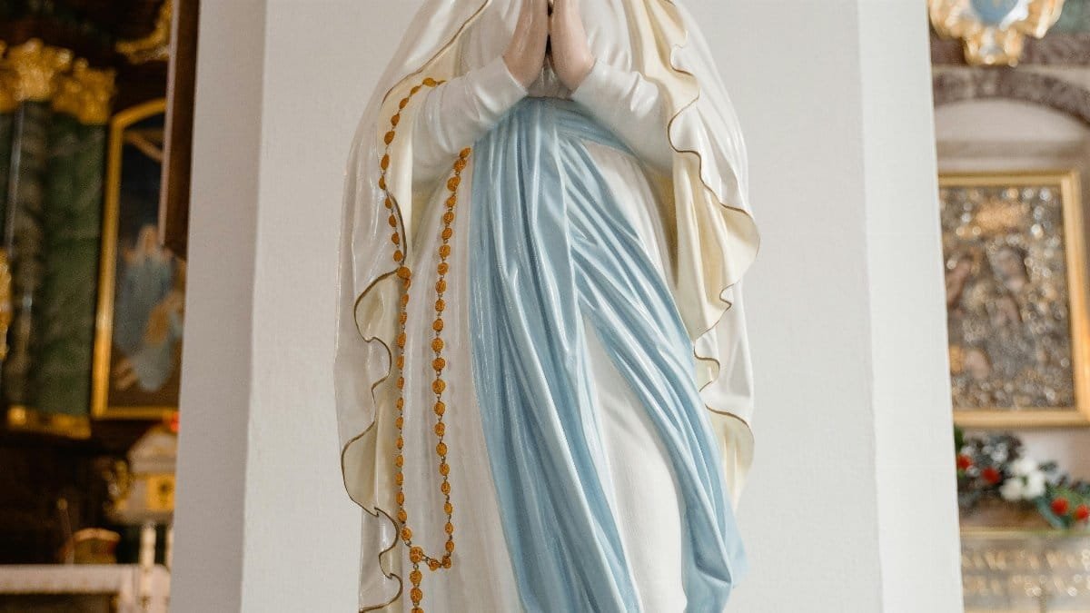 A serene statue of the Virgin Mary with a rosary, praying inside a beautiful church. via Pexels