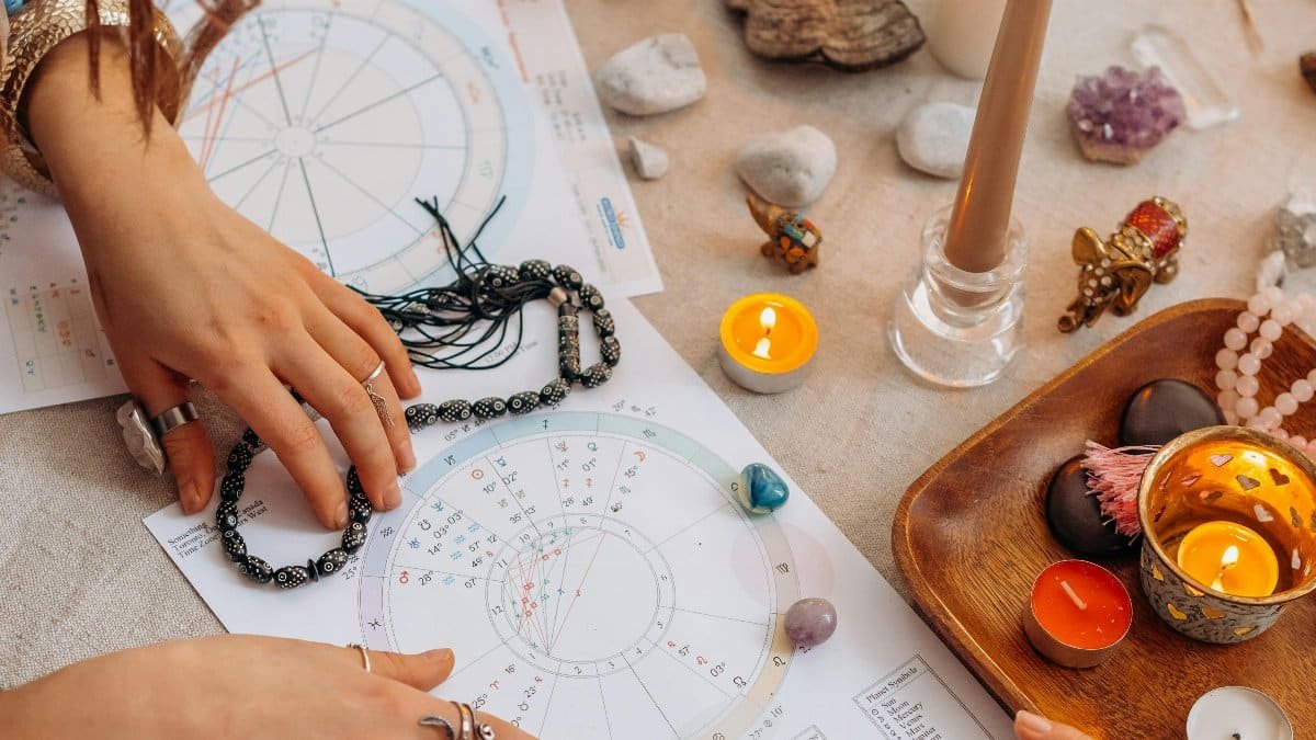 Hands arranging astrology charts with candles and crystals on a table for a spiritual ritual. via Pexels