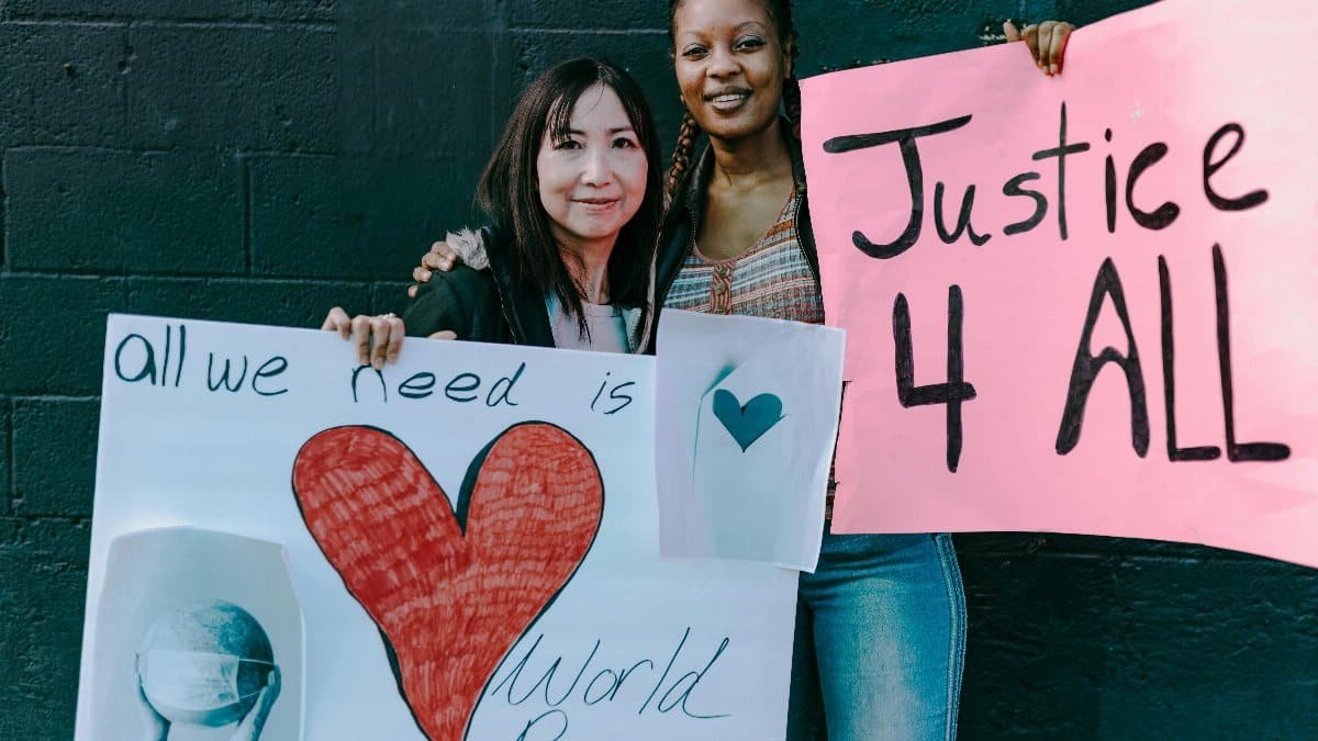 Two women holding signs for world peace and justice at a demonstration. via Pexels