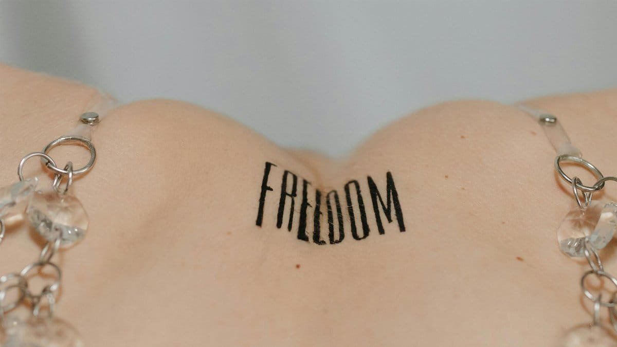 Artistic close-up of a 'Freedom' tattoo on a human back adorned with crystal chain. via Pexels
