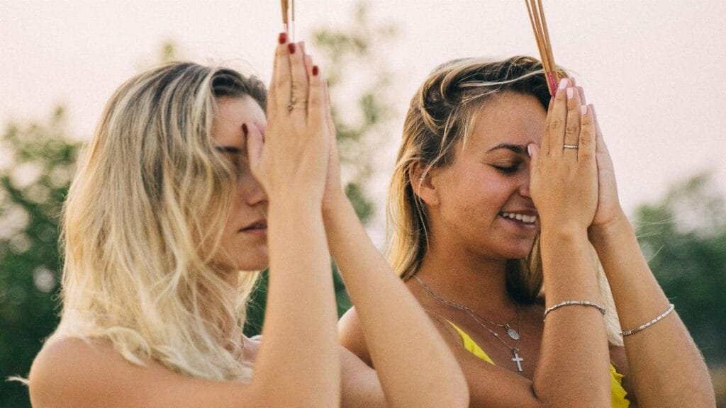 Two women meditating with incense outdoors, embracing summer tranquility. via Pexels