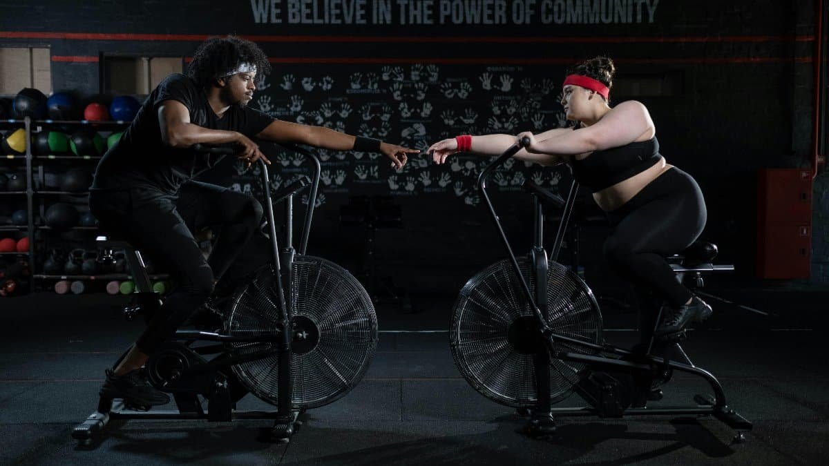 Two diverse individuals connect and motivate each other during a workout session on stationary bikes in a gym. via Pexels