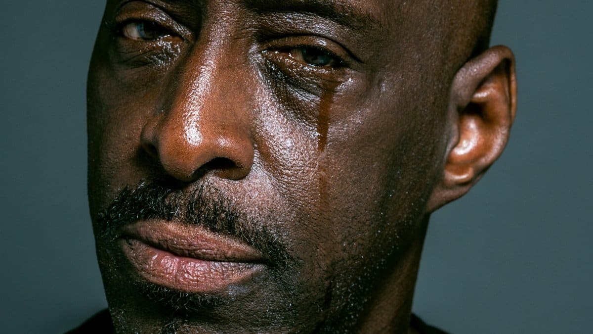 A close-up portrait of a man shedding a tear against a gray background, depicting sadness and contemplation. via Pexels