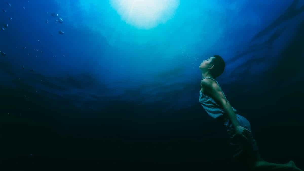 A serene scene of a person swimming underwater towards sunlight, capturing tranquility and exploration. via Pexels