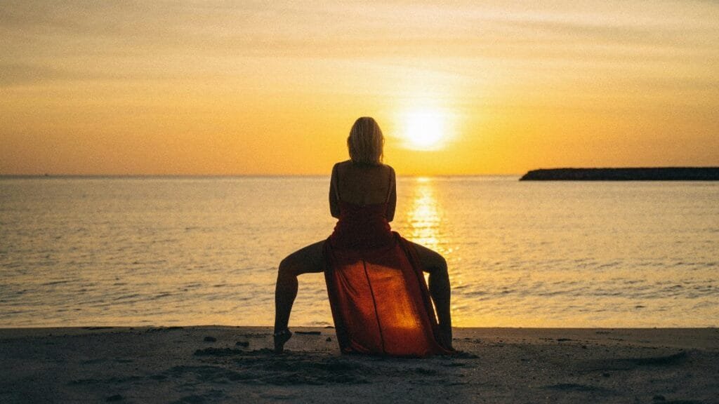 A woman in a red dress performs yoga at sunset on a serene beach. via Pexels