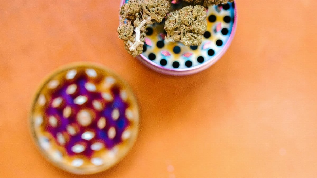 Top view of marijuana buds on a colorful grinder against an orange surface, emphasizing cannabis culture. via Pexels