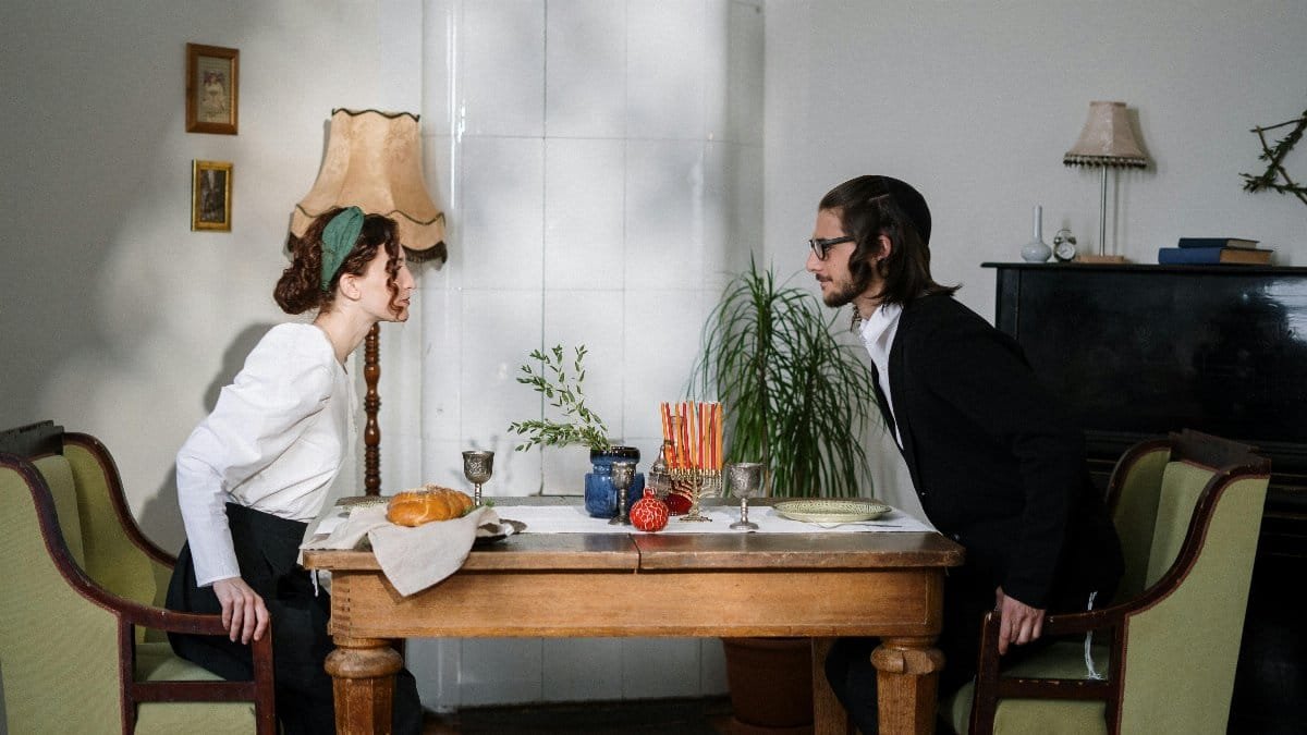 Jewish couple enjoying a traditional Hanukkah meal at home with a warm, cozy ambiance. via Pexels