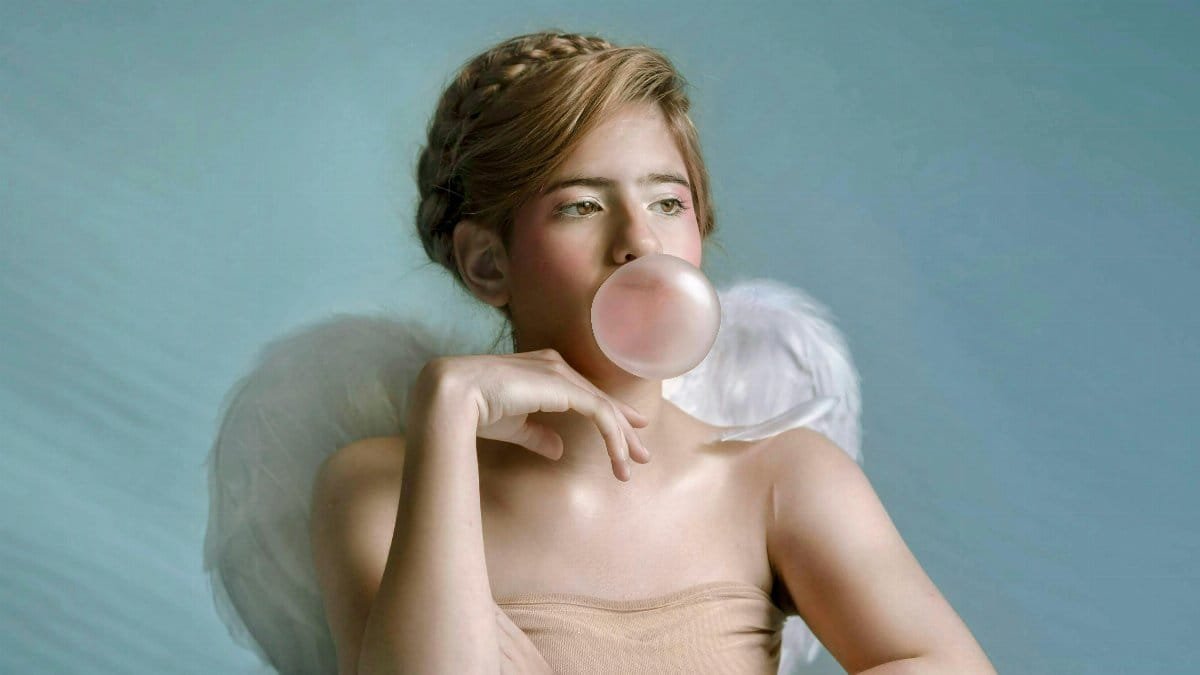 Artistic portrait of a teenage angel blowing bubble gum with ethereal lighting. via Pexels