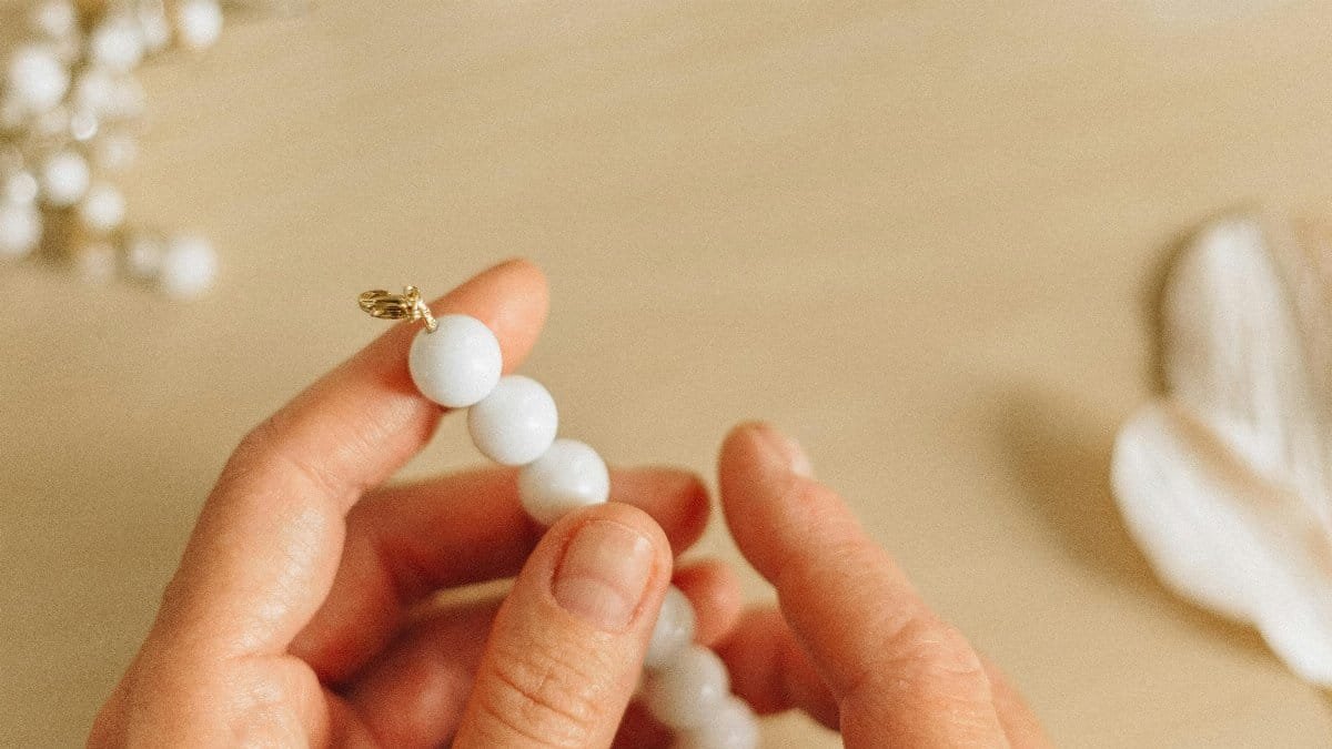 Close-up of hands crafting handmade bead necklace on a wooden surface. via Pexels
