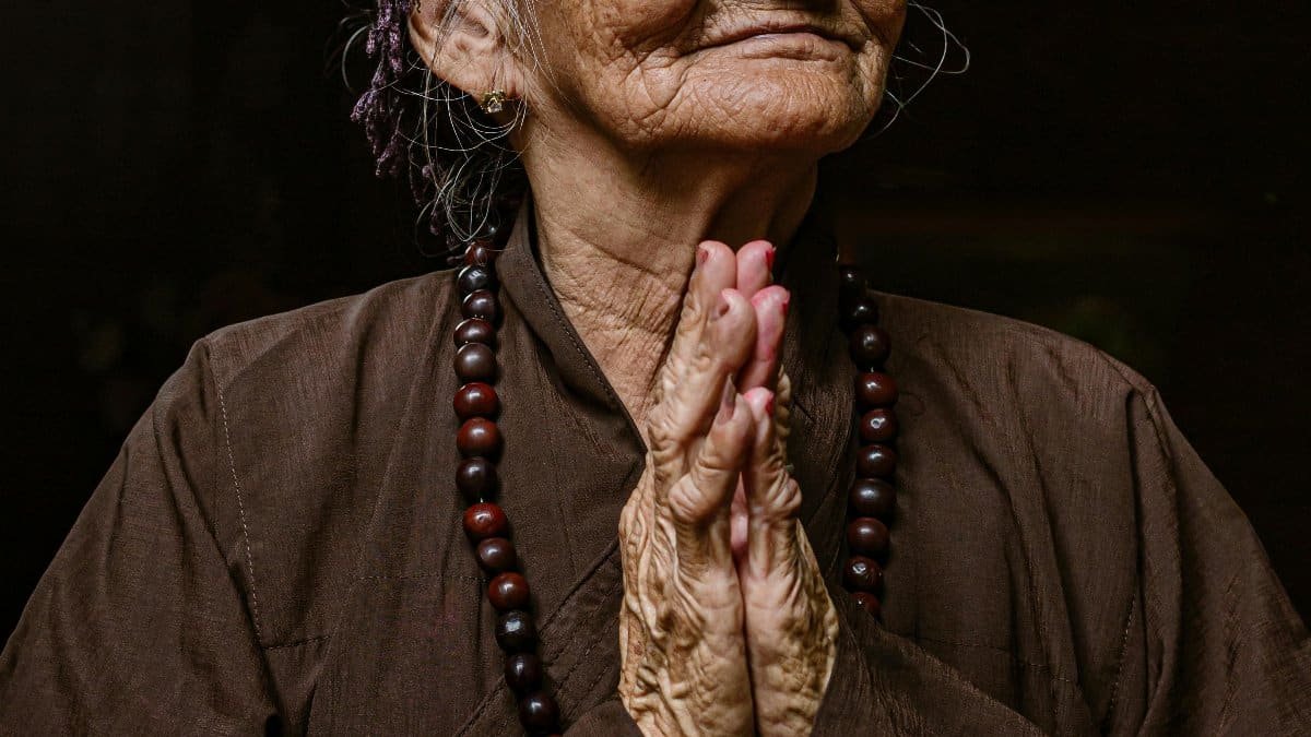 Elderly Vietnamese woman in traditional clothing, praying and smiling, showcasing cultural heritage. via Pexels