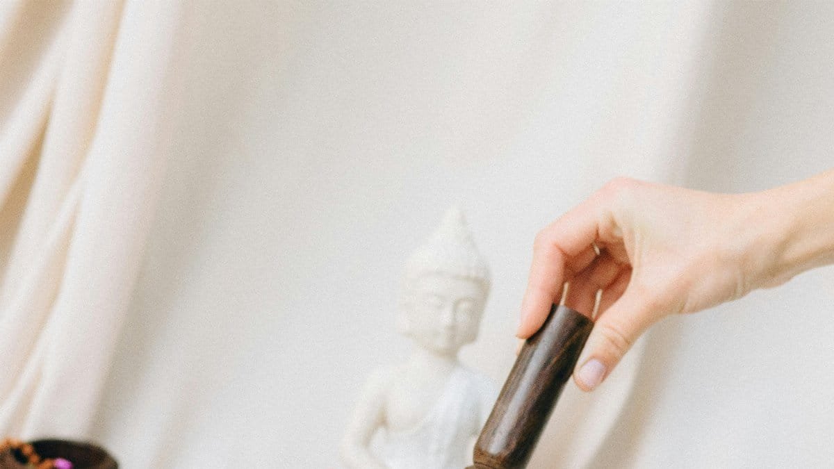 A serene setup featuring a hand using a singing bowl beside a Buddha statue, perfect for meditation. via Pexels