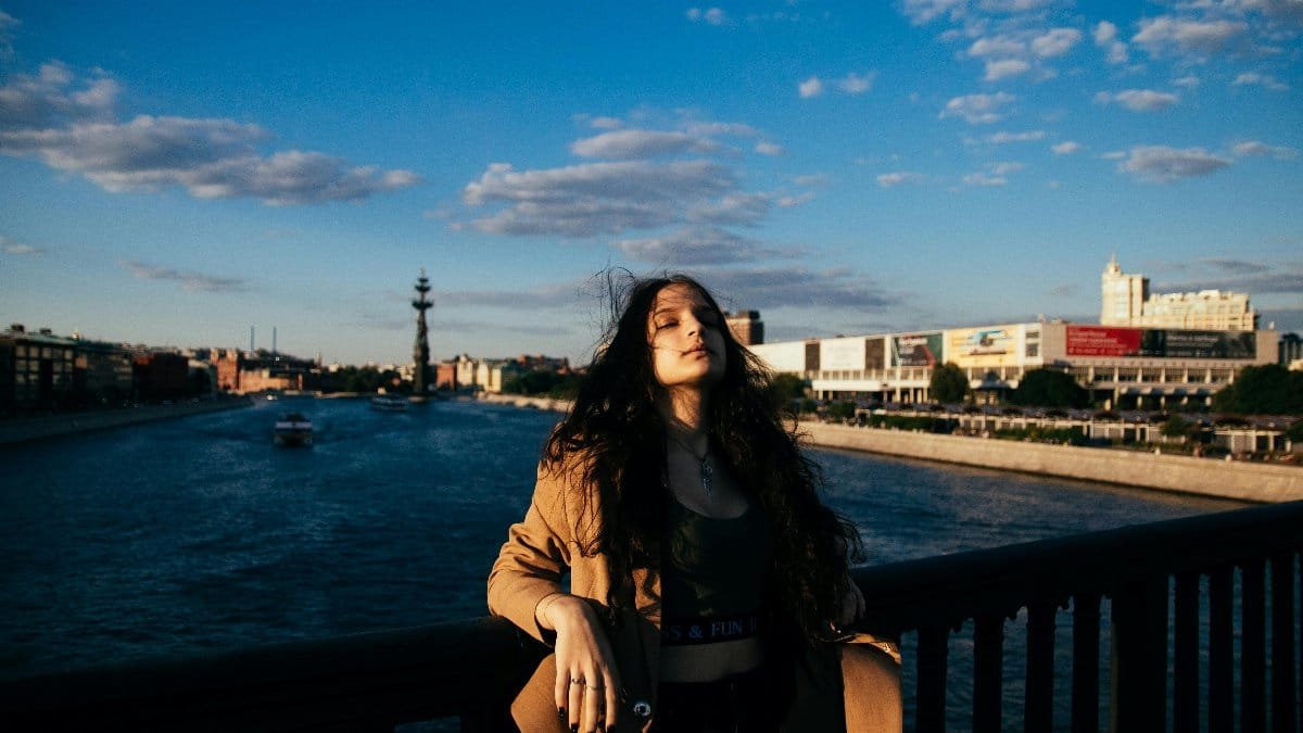 A woman with eyes closed enjoys the sunset on a bridge, capturing a serene moment. via Pexels