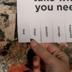 A hand holding a paper note taped on a brick wall with motivational words to pick from. via Pexels
