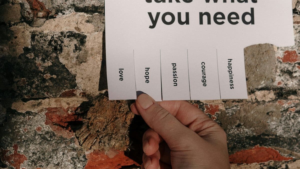 A hand holding a paper note taped on a brick wall with motivational words to pick from. via Pexels