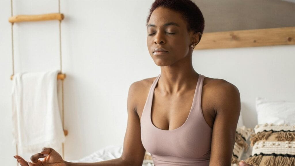 Woman practicing meditation on a bed, focusing on wellness and tranquility indoors. via Pexels