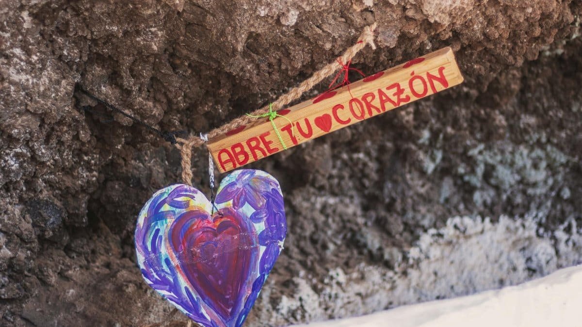 Vibrant heart artwork with a Spanish message on wood, urging love and connection.