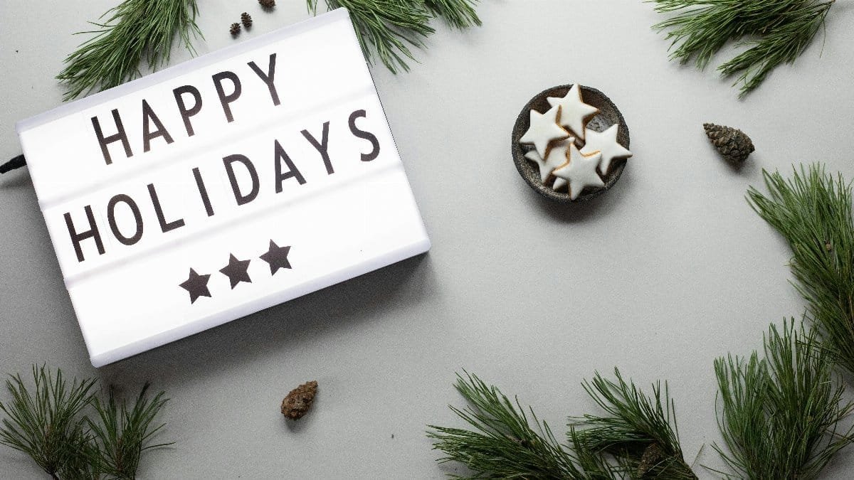 Top view of a festive holiday setup with star cookies, pine branches, and a 'Happy Holidays' sign.