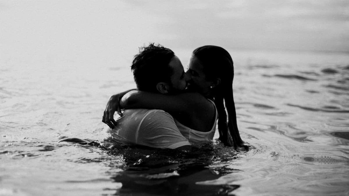 A romantic embrace and kiss in the ocean, captured in black and white.