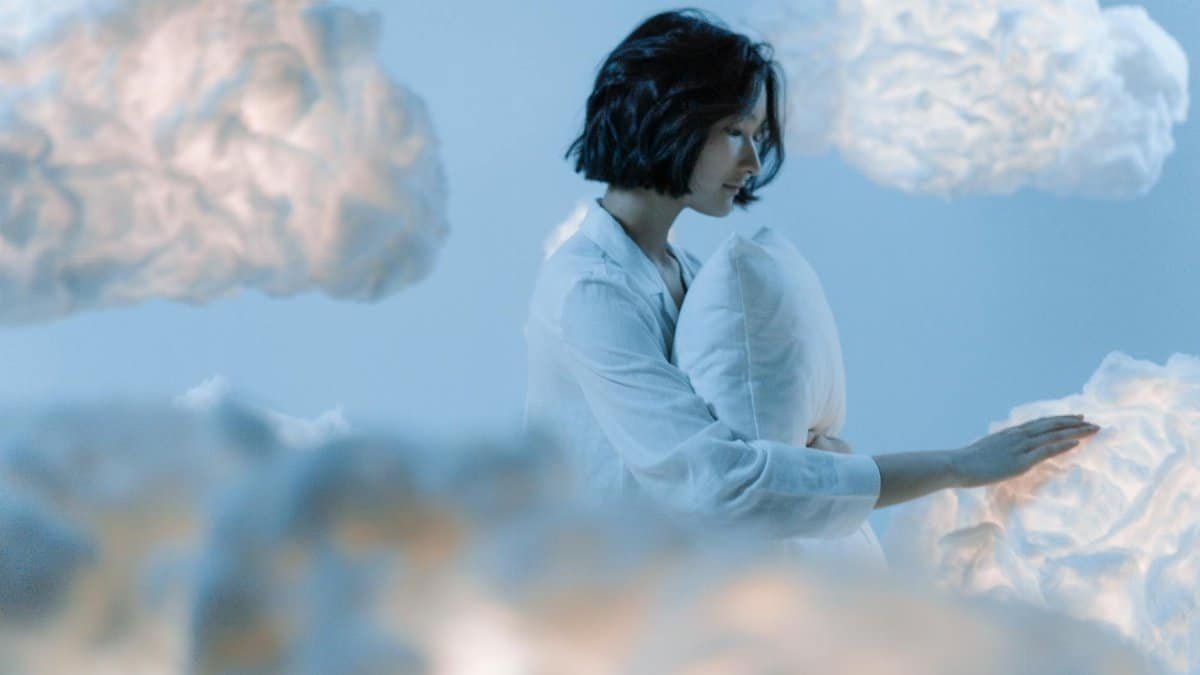 A serene scene of an Asian woman dreaming among soft, ethereal clouds.