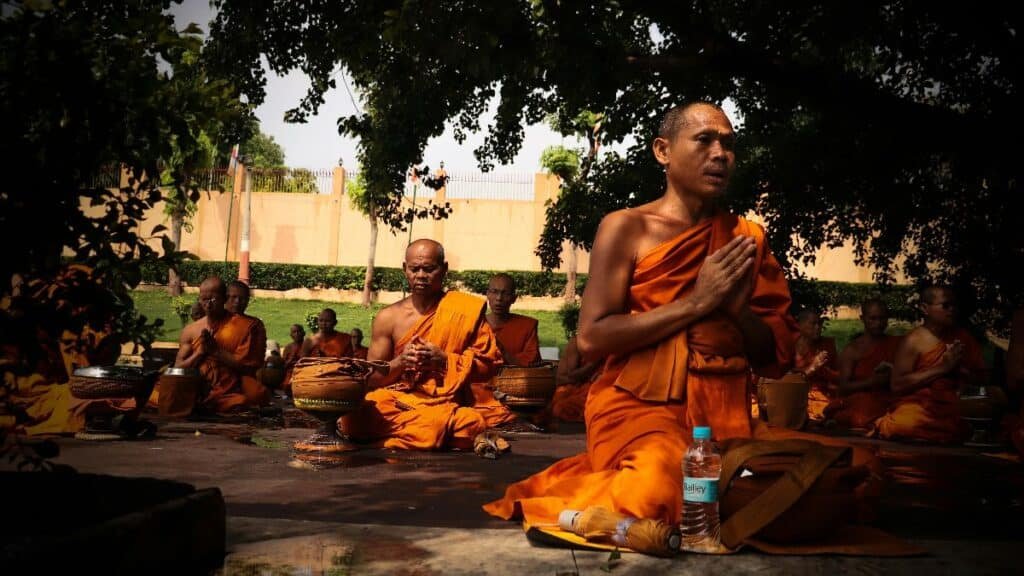 Group of monks meditating outdoors in traditional orange robes, focused in deep contemplation.
