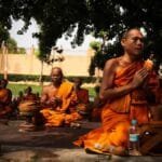 Group of monks meditating outdoors in traditional orange robes, focused in deep contemplation.