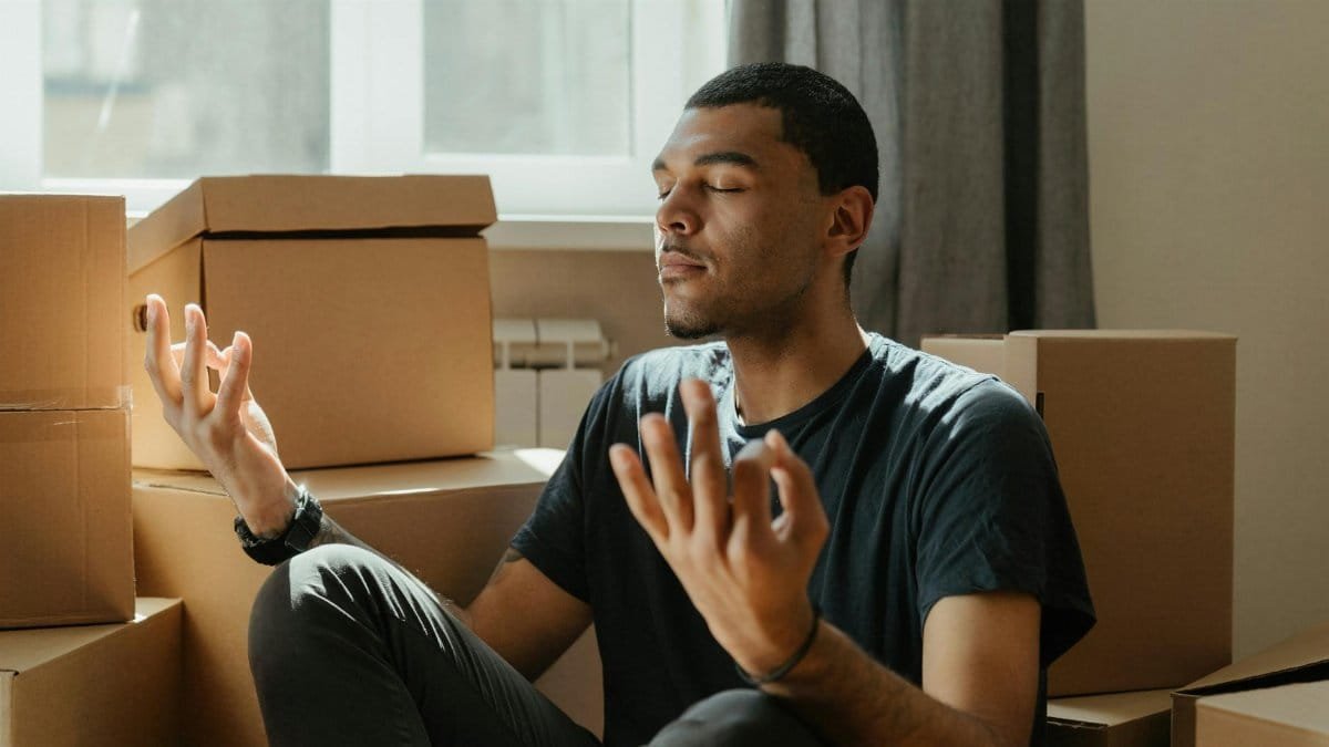 A young man practices meditation surrounded by cardboard boxes during a move.