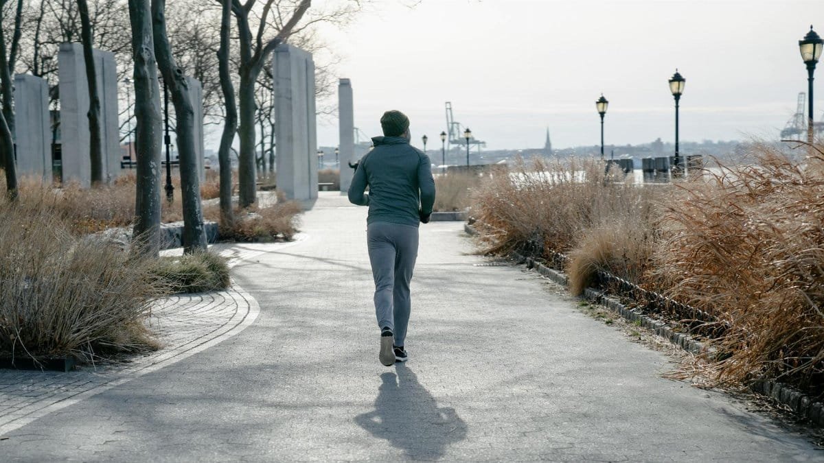 A man jogging through a tranquil urban park on an autumn morning, embracing nature and wellness.