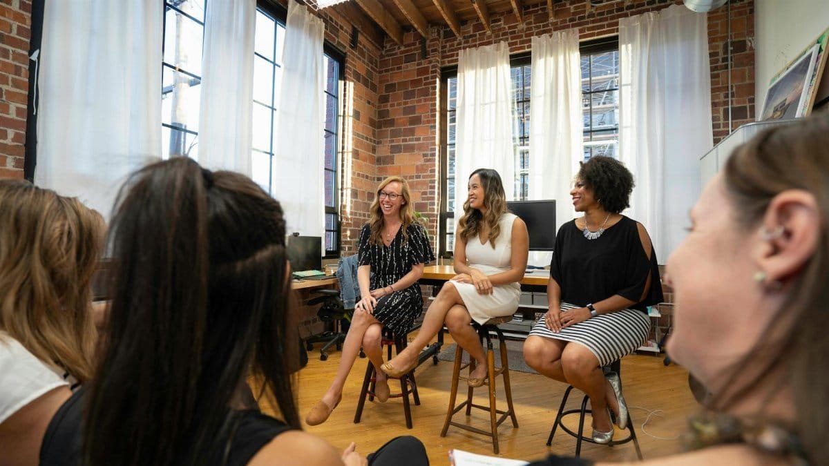 Women engaging in a panel discussion in a modern office setting, fostering an inclusive business community.