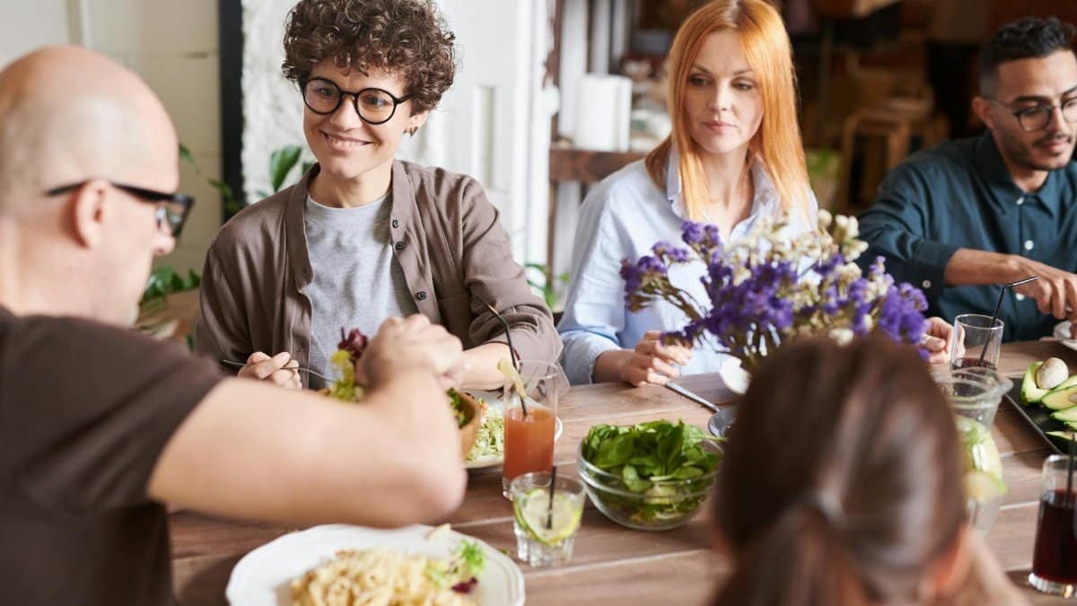A diverse group of friends dining together at a cozy indoor setting, sharing and enjoying a meal.