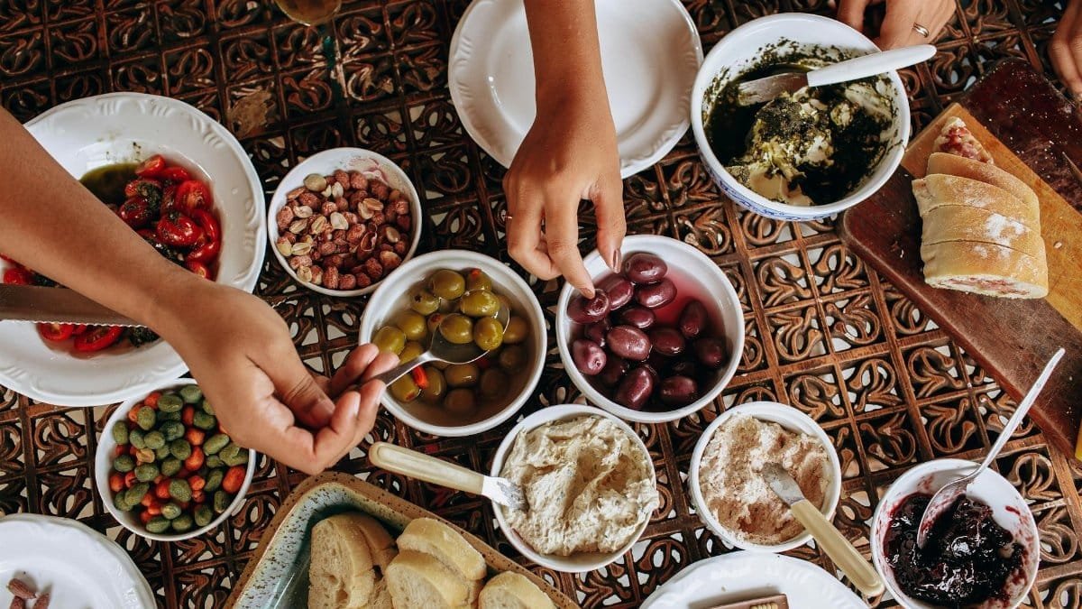 Overhead view of a rustic Mediterranean meal setup with diverse dishes and hands reaching.