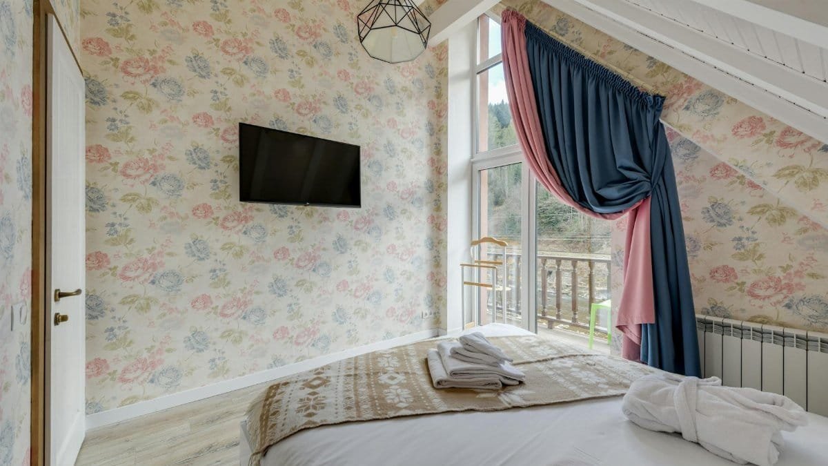 Bright bedroom featuring floral wallpaper, exposed beams, and a view of the balcony.