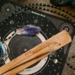 Astrology-themed flat lay featuring a birthdate book, crystals, and necklace on a wooden surface.