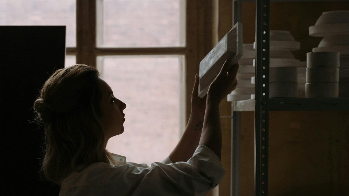 An artisan organizing ceramic plates on shelves against a distant window.