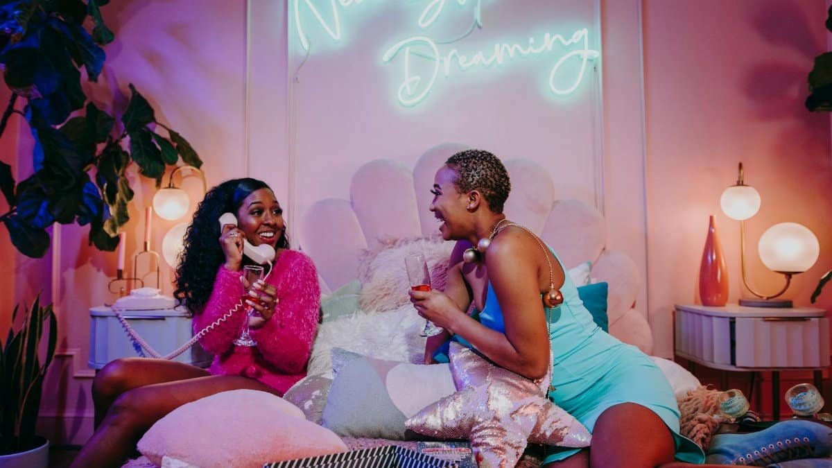 Two women enjoying a cozy indoor pajama party with a neon 'Never Stop Dreaming' sign.