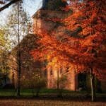 Charming view of a historic church surrounded by vibrant autumn foliage under clear skies.