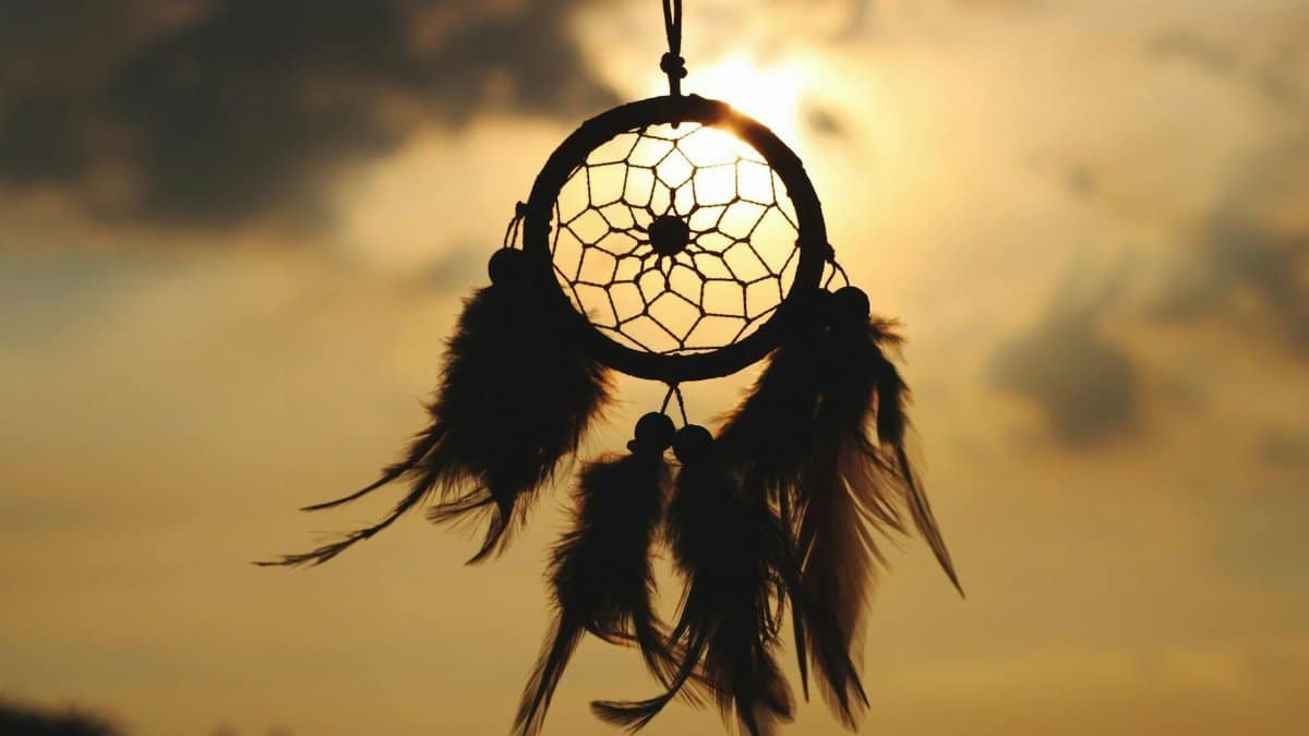 Silhouette of a dreamcatcher hanging against a serene sunset sky.