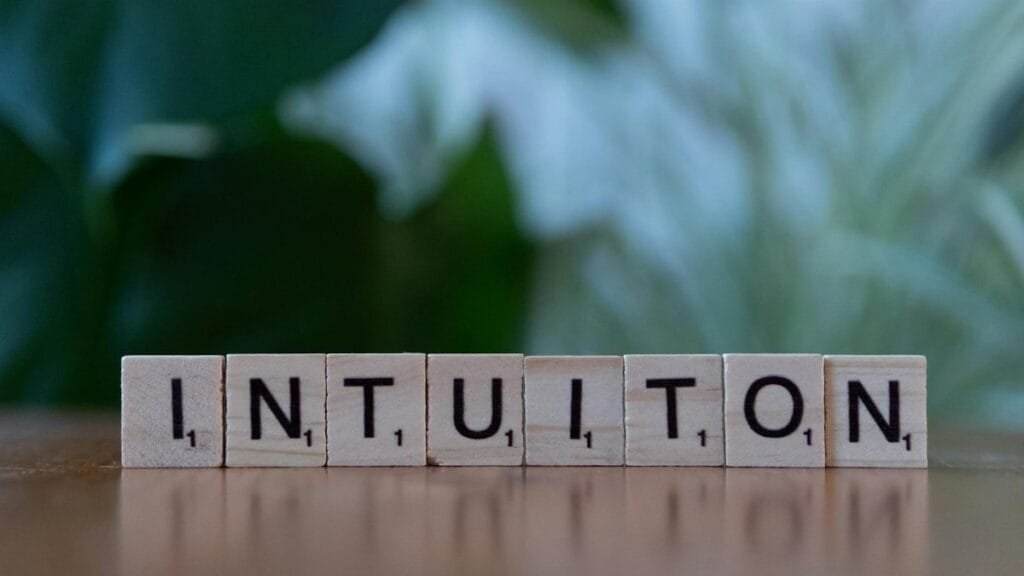 Wooden letter tiles spelling 'Intuition' on a blurred green background.