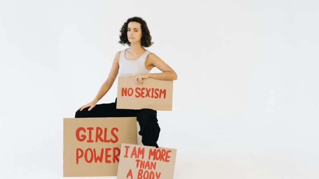 Woman holding protest signs advocating against sexism and promoting gender equality.