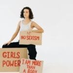 Woman holding protest signs advocating against sexism and promoting gender equality.