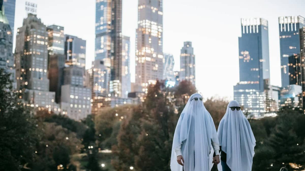 Two people in ghost costumes with sunglasses in a city park at night.