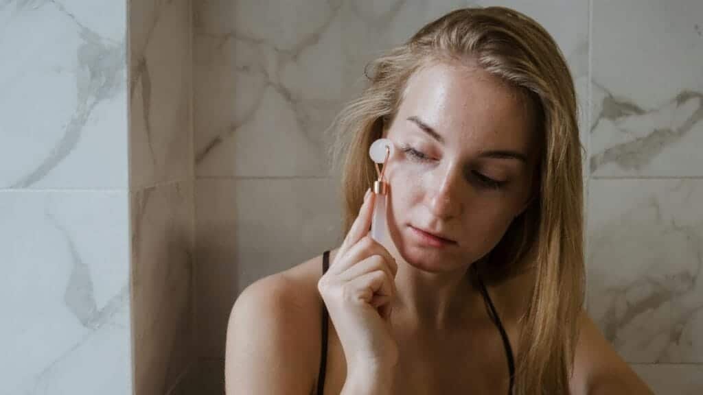 A woman using a jade roller on her face as part of her skincare routine.