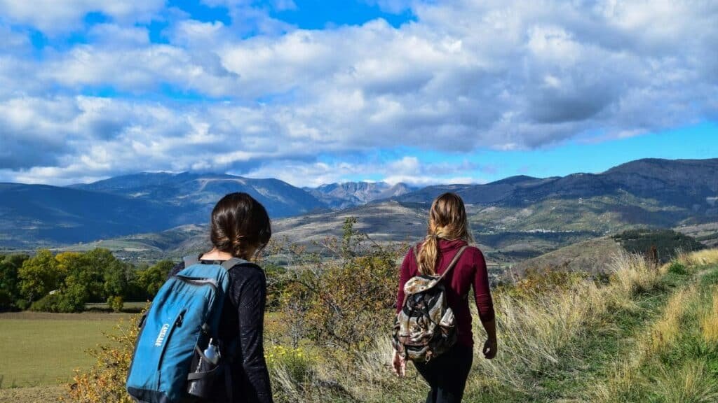 Two women hiking on a mountain trail with scenic views under a blue sky.